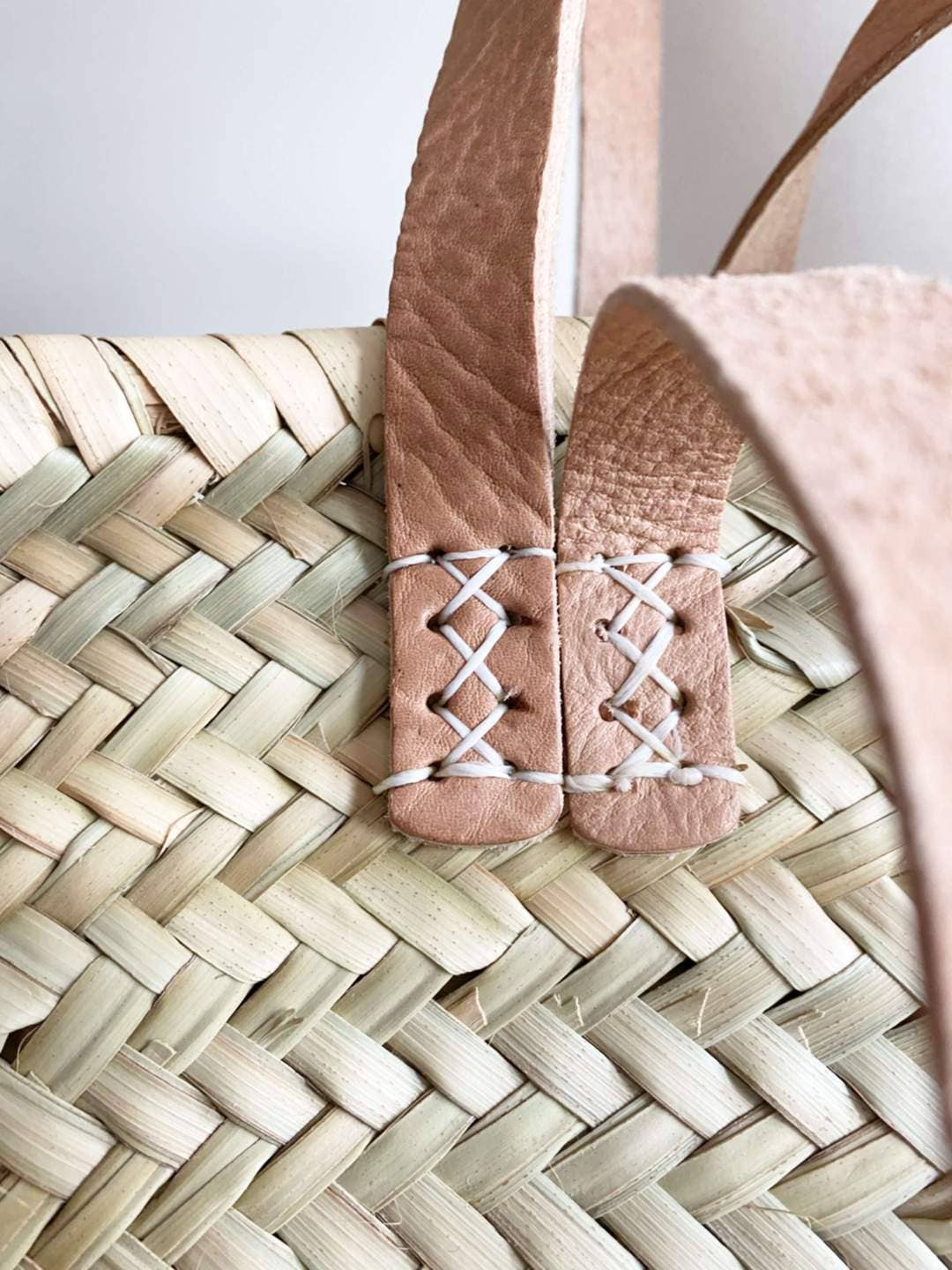 Close-up of a woven french market basket with a brown leather strap and the nice-looking seam.