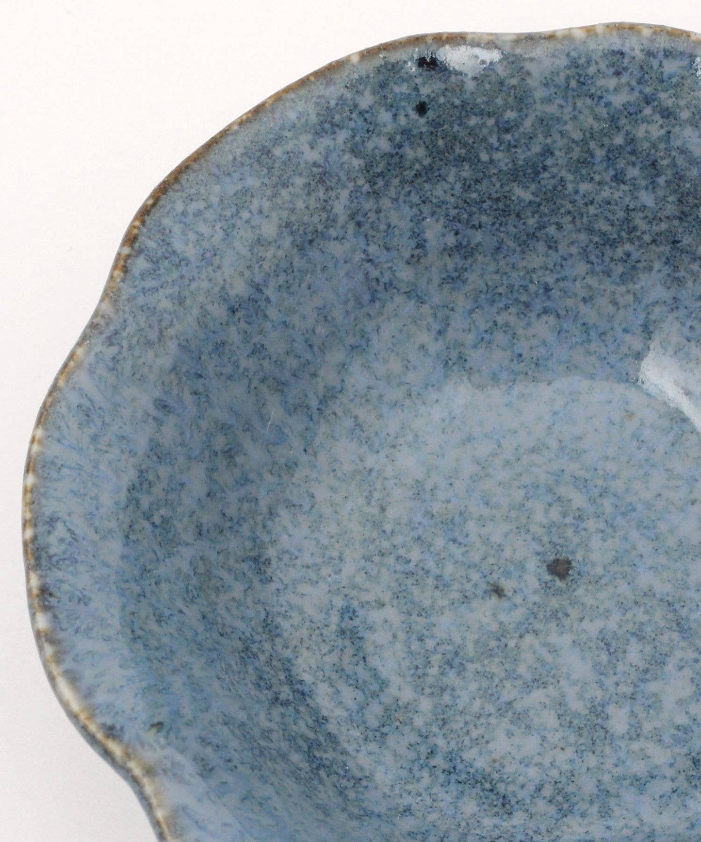 Close-up on a ceramic mino ware mini bowl with a flower shape and a soft blue speckled glazed finishe on a white background.