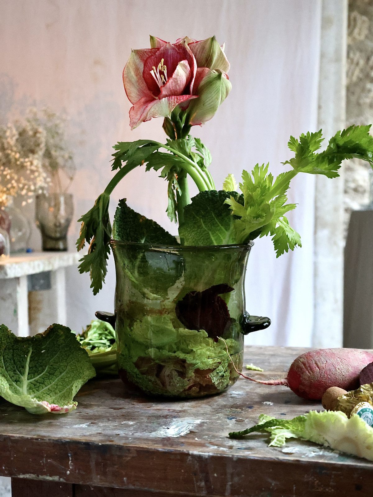 Decorative arrangement with a flower and leaves in a handmade glass container on a wooden surface.