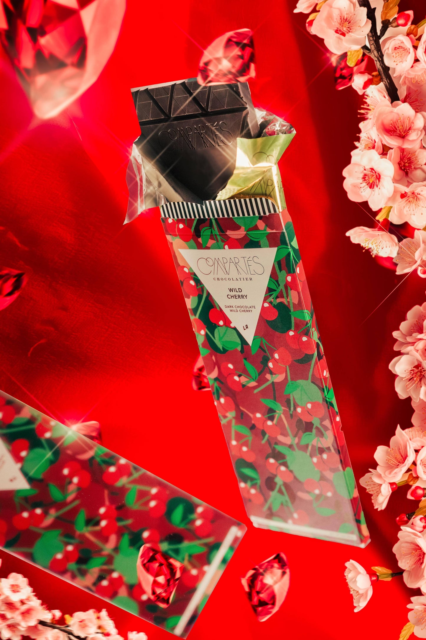 A gourmet dark chocolate bar with visible pieces of cherries embedded in it, presented on a bright red background with cherry blossoms.
