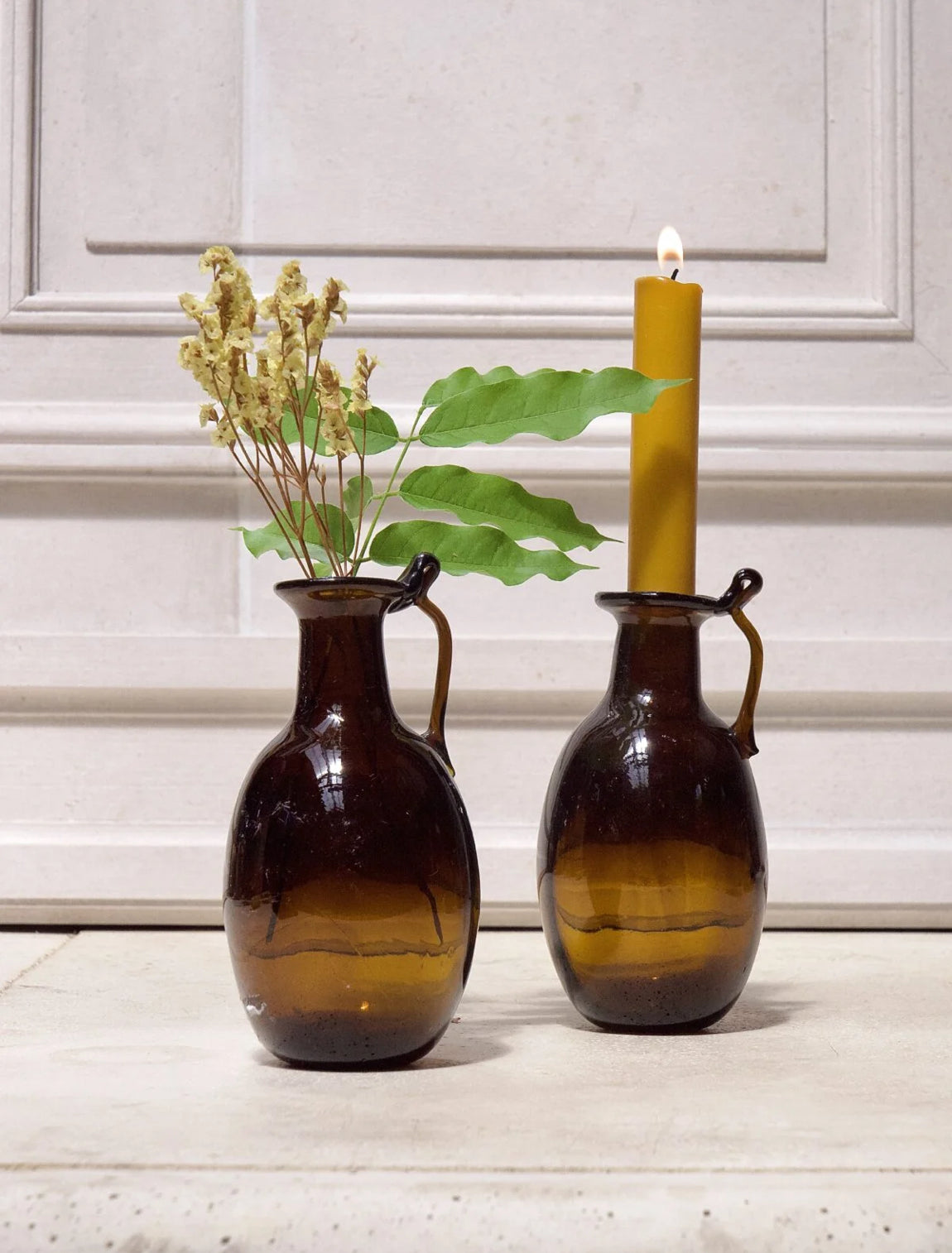 Two brown vases with a candle and plant on a light background