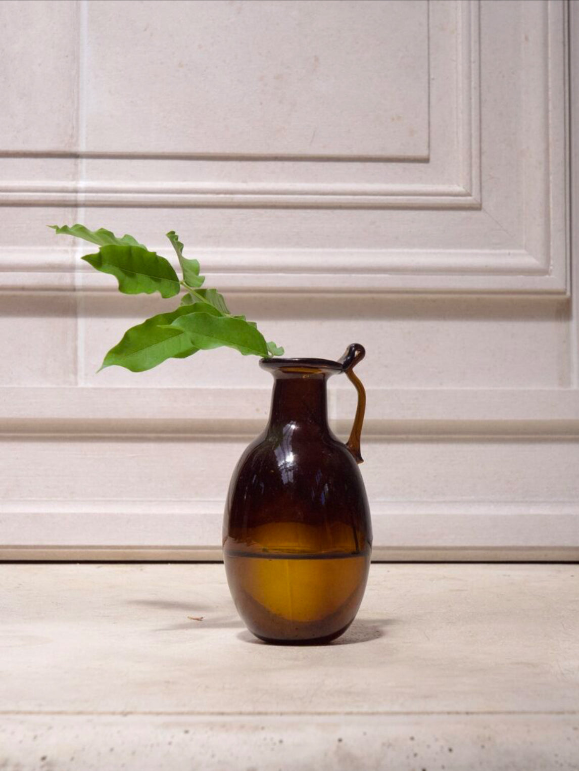 Brown mouth-blown glass vase with a plant on a wooden surface