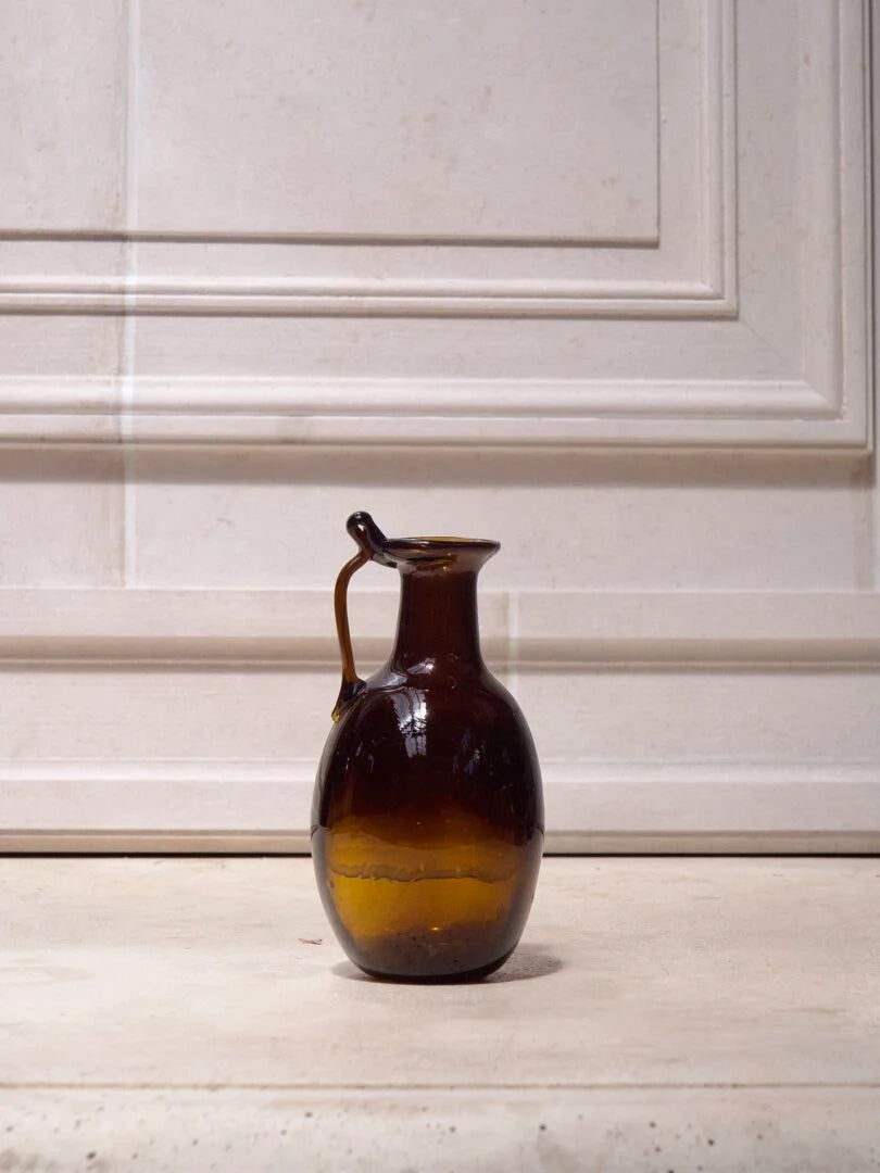Artisanal brown glass jug on a light wooden surface with a white cabinet background