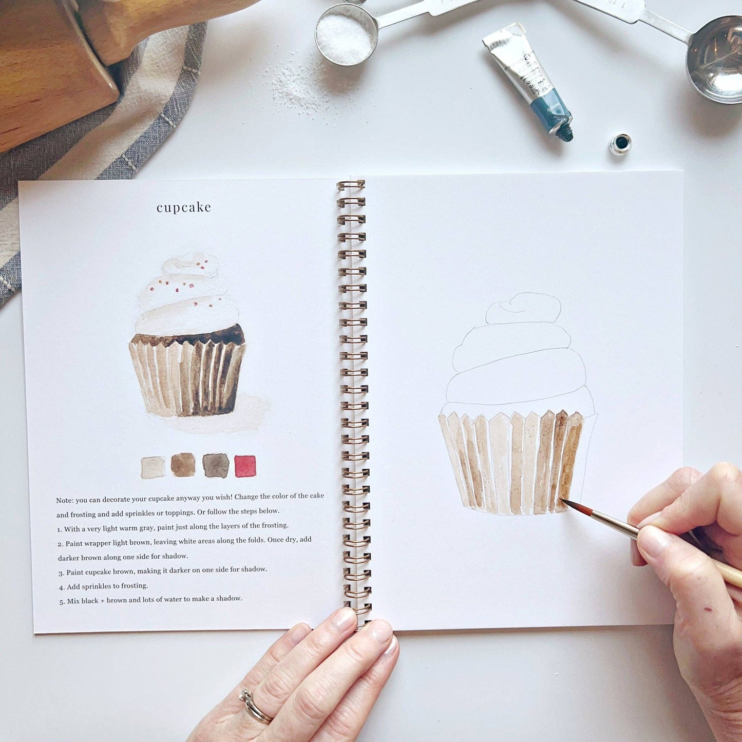 Creative watercolor activity book with step-by-step baking-themed sketches, here on the cupcake page