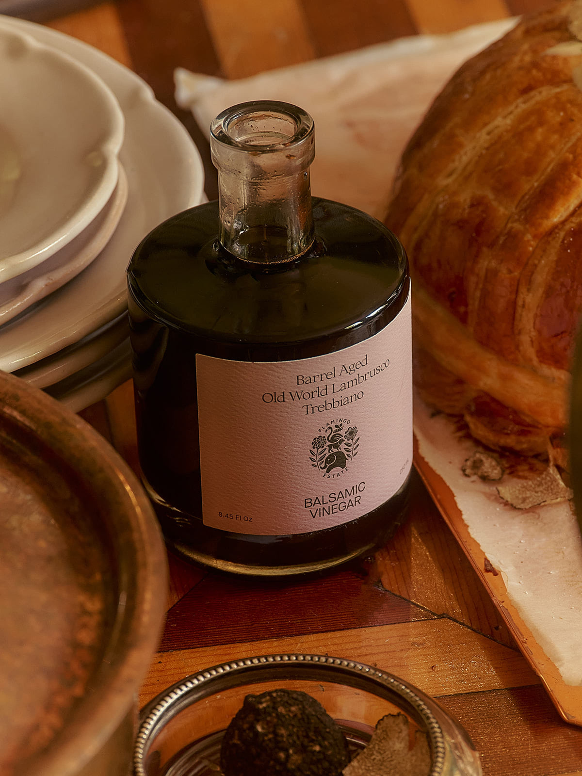 Balsamic vinegar bottle on a wooden surface with bread and plates in the background