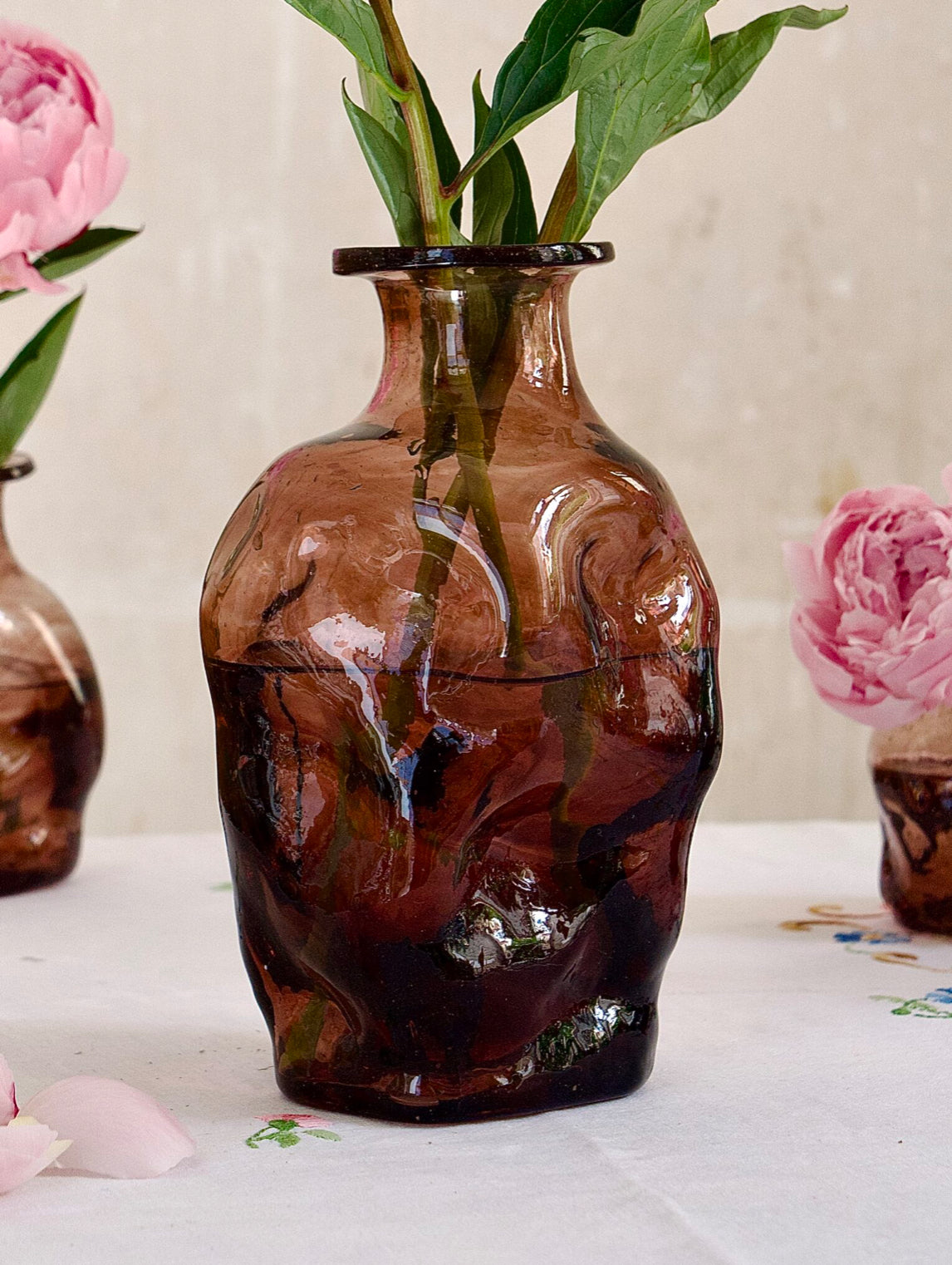 Brown and raspberry-hued recycled glass vase with a sculptural form and flowers on a light surface

