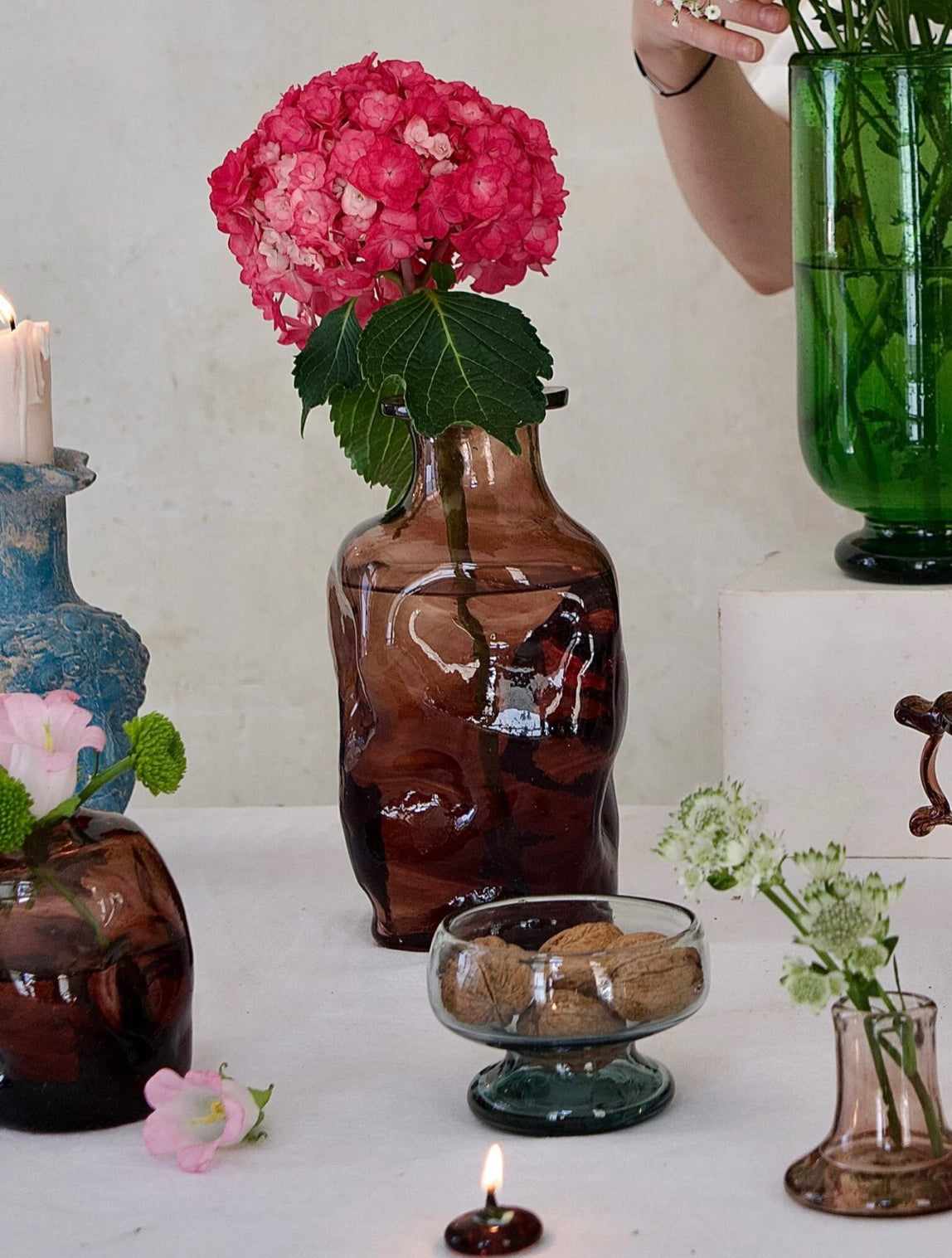 Decorative table setting with various mouth-blown vases and flowers on a white surface.