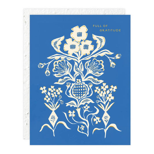 A blue greeting card with a white floral pattern and text that reads 'FULL OF GRATITUDE'. It has foil details and is accompanied by a plantable seed paper envelope.