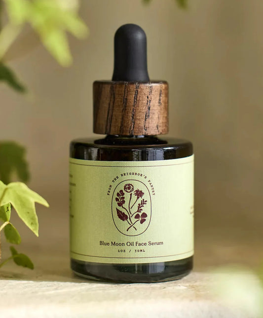 Bottle of Blue Moon Oil Face Serum with wooden dropper on a blurred natural background