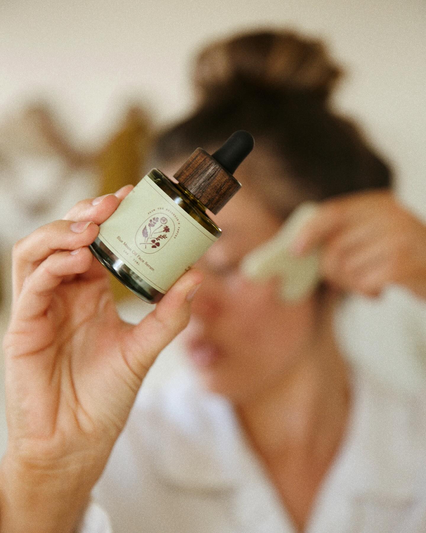 Person holding a dropper bottle of the Blue Moon Face serum from My Neighbor's with a blurred background