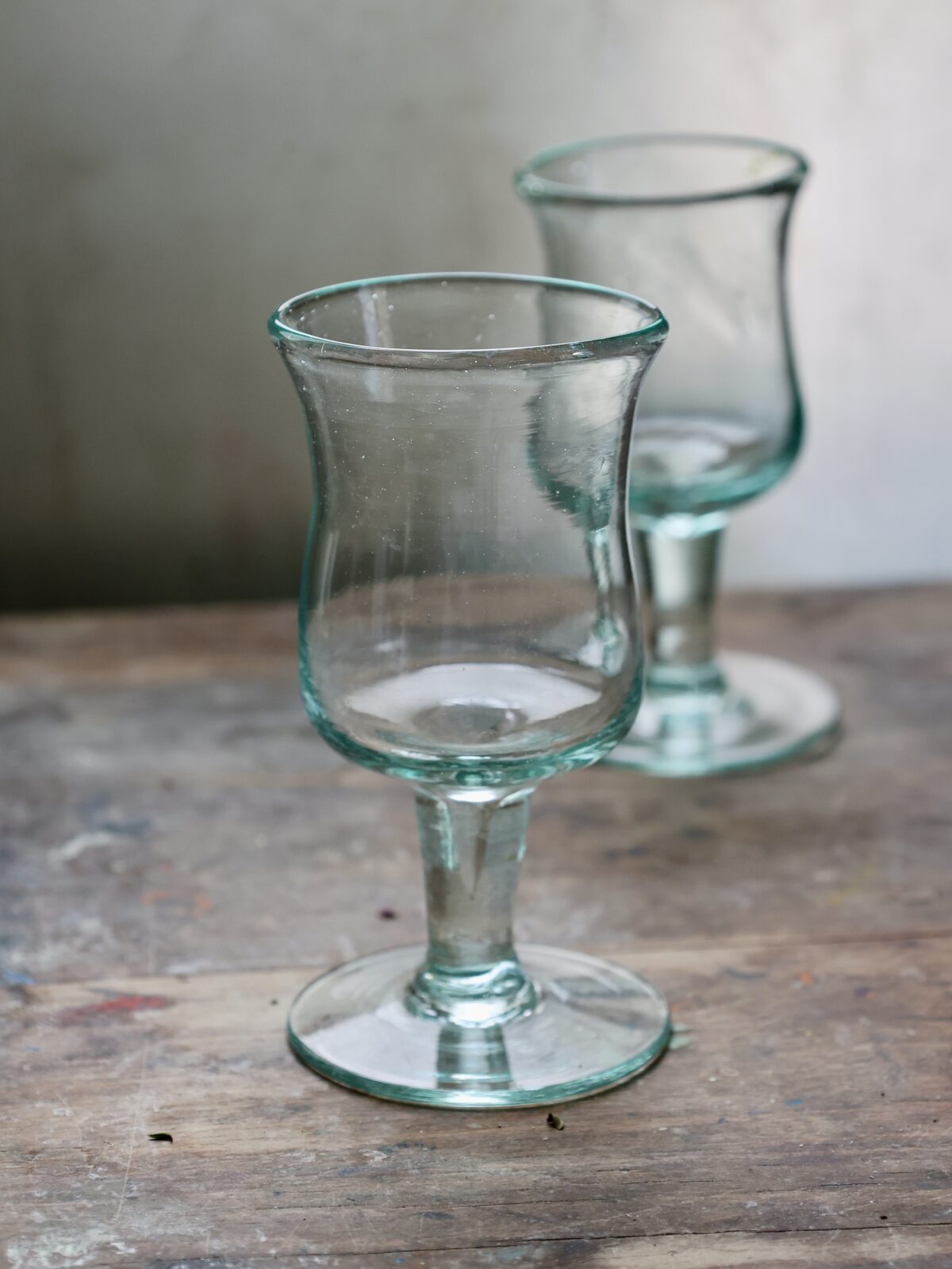 Two clear handmade Bordeaux wine glass with curved design on a wooden surface with a blurred background