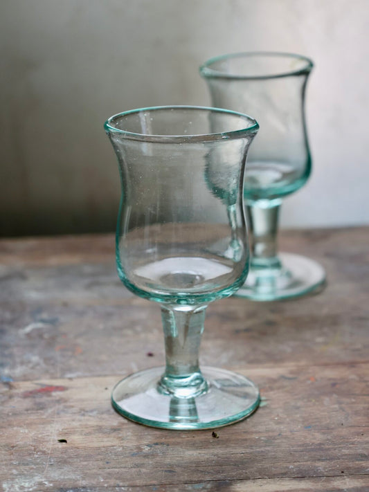 Two clear handmade Bordeaux wine glass with curved design on a wooden surface with a blurred background