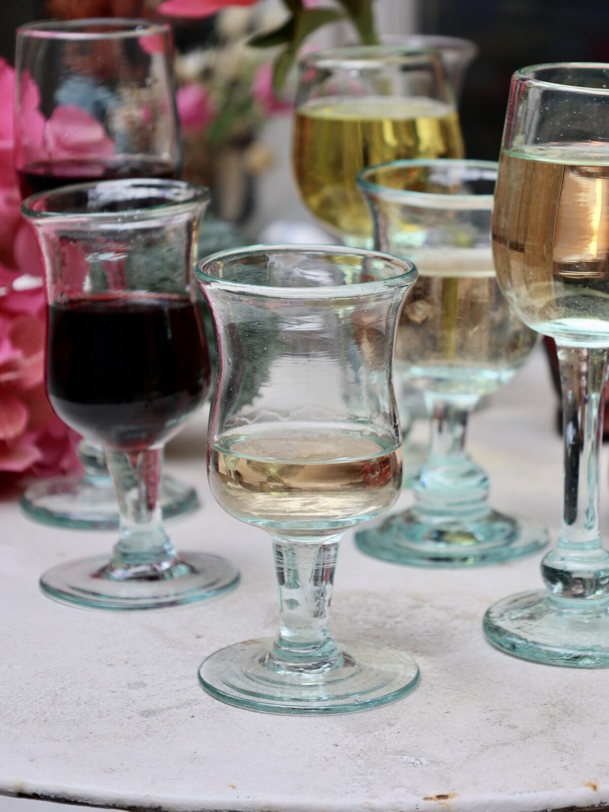 Elegant transparent French mouth-blown glassware with different wines on a table with flowers in the background