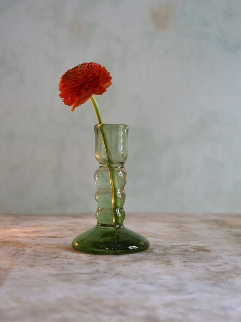 Small artisan-made green glass bud vase with bubble design and a single red flower on a marble surface