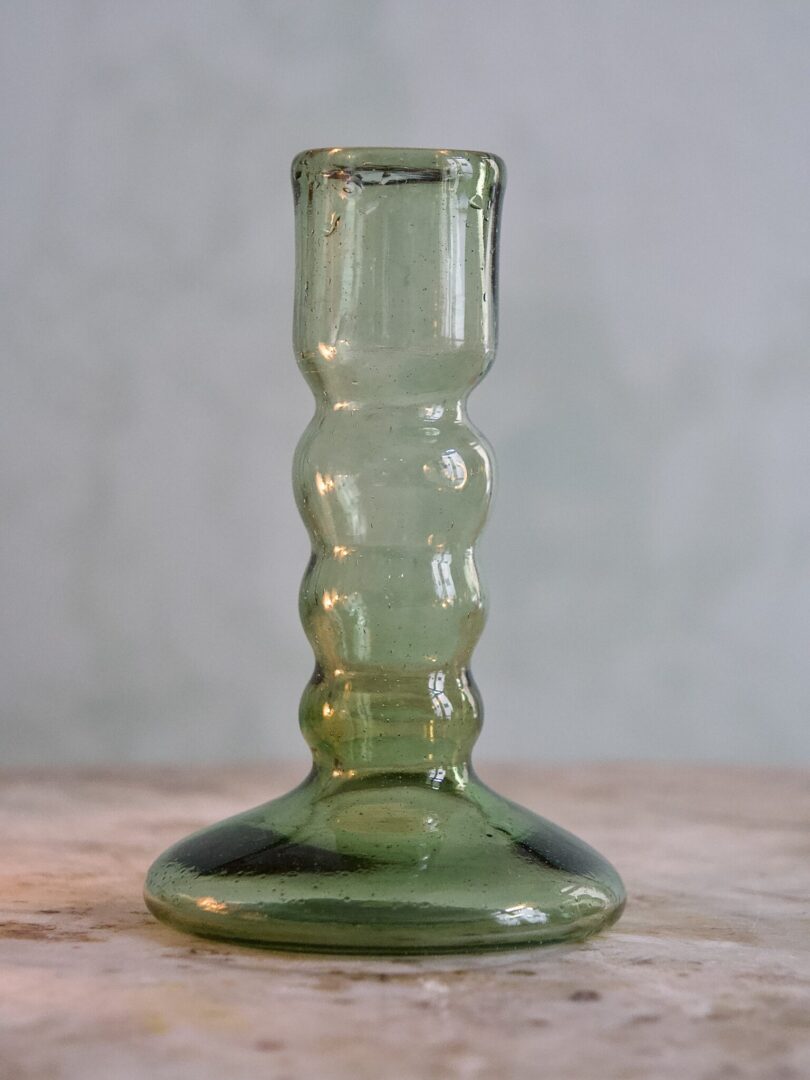 Elegant handmade smoky green glass candle holder on a wooden surface with a gray background
