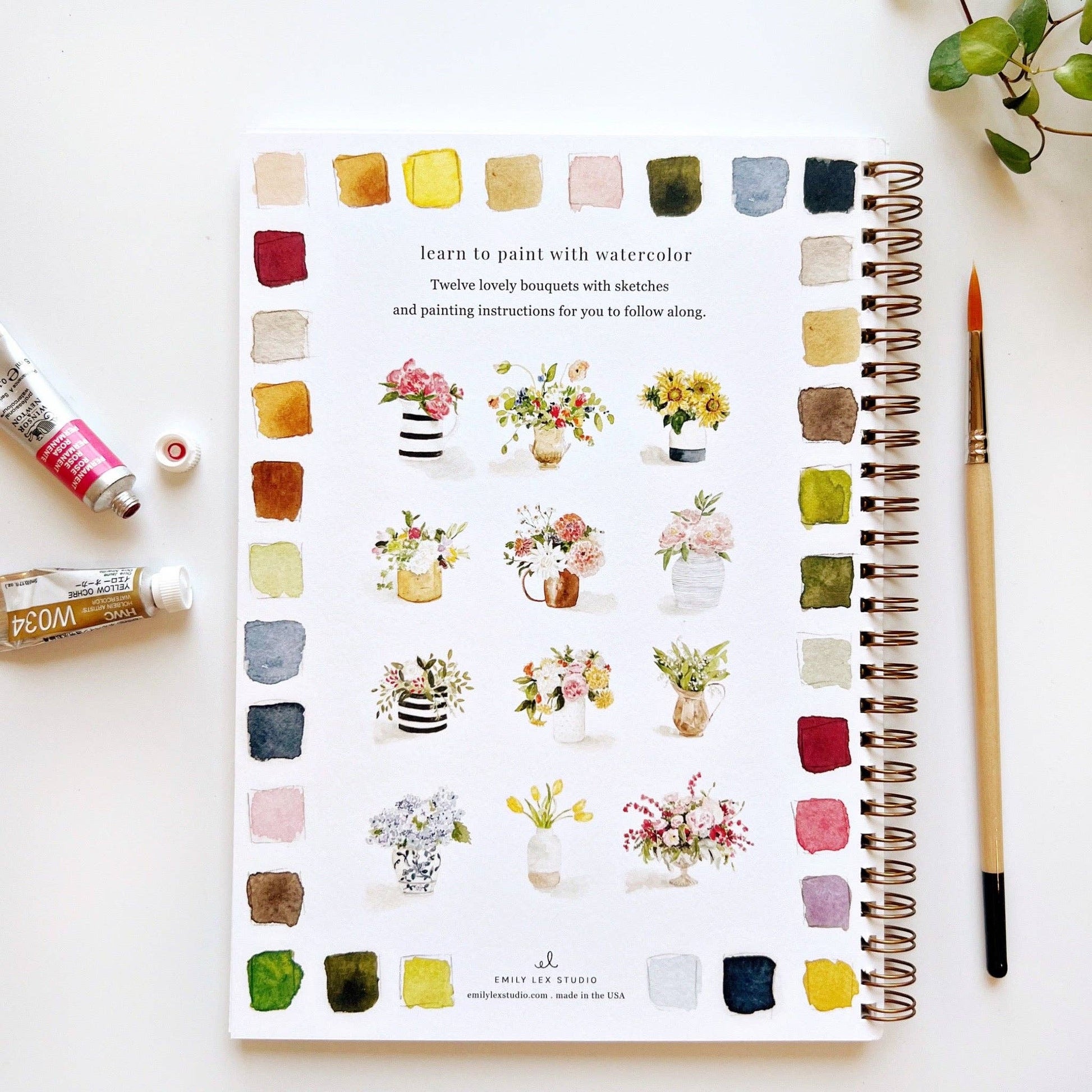 Creative watercolor workbook with watercolor flower illustrations and painting tools on a white surface