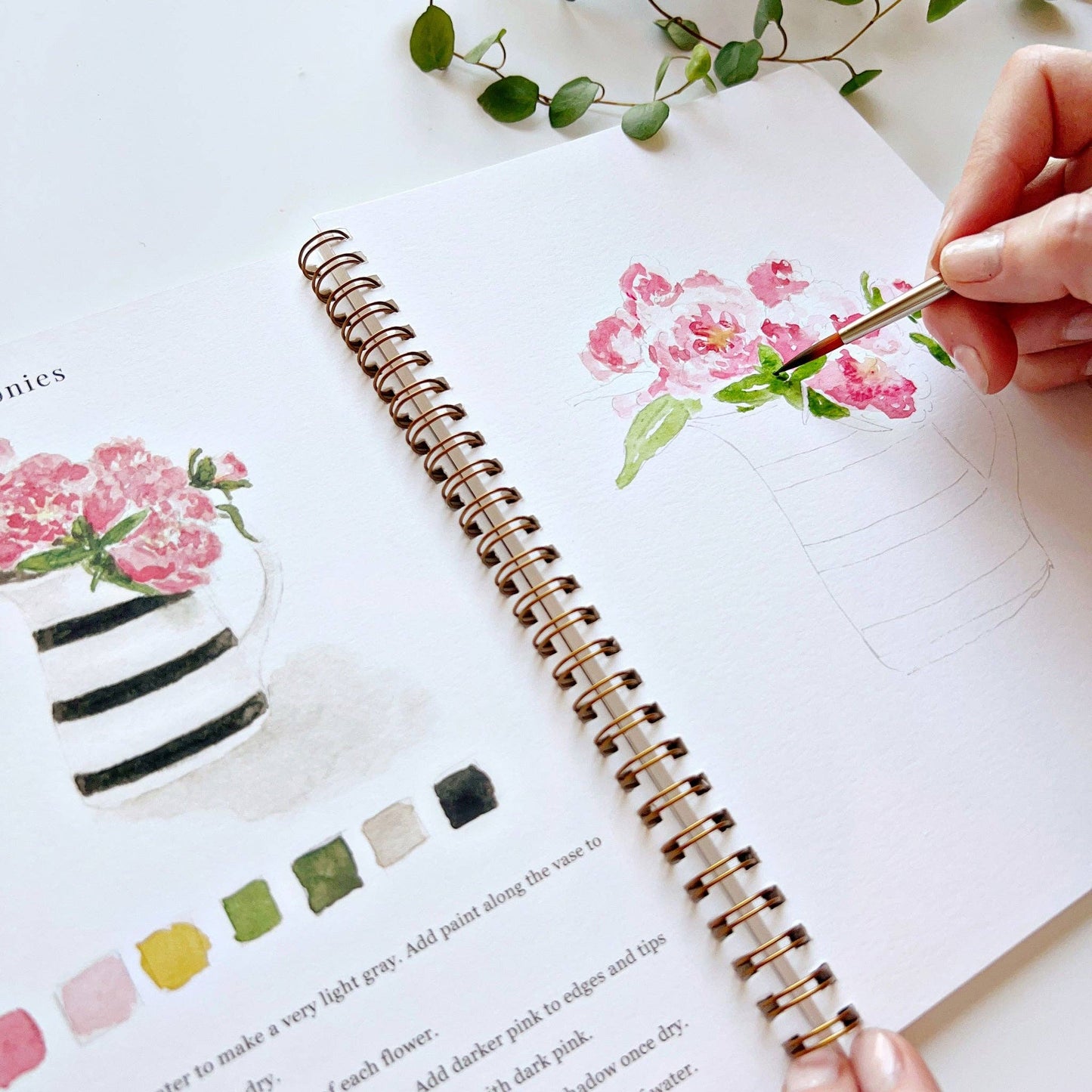 Person painting flowers bouquets on a watercolor workbook with a paintbrush