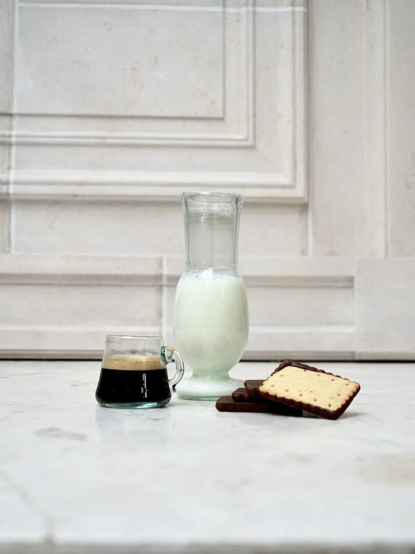 Glass of milk, coffee, and cookies on a marble countertop with white cabinets.