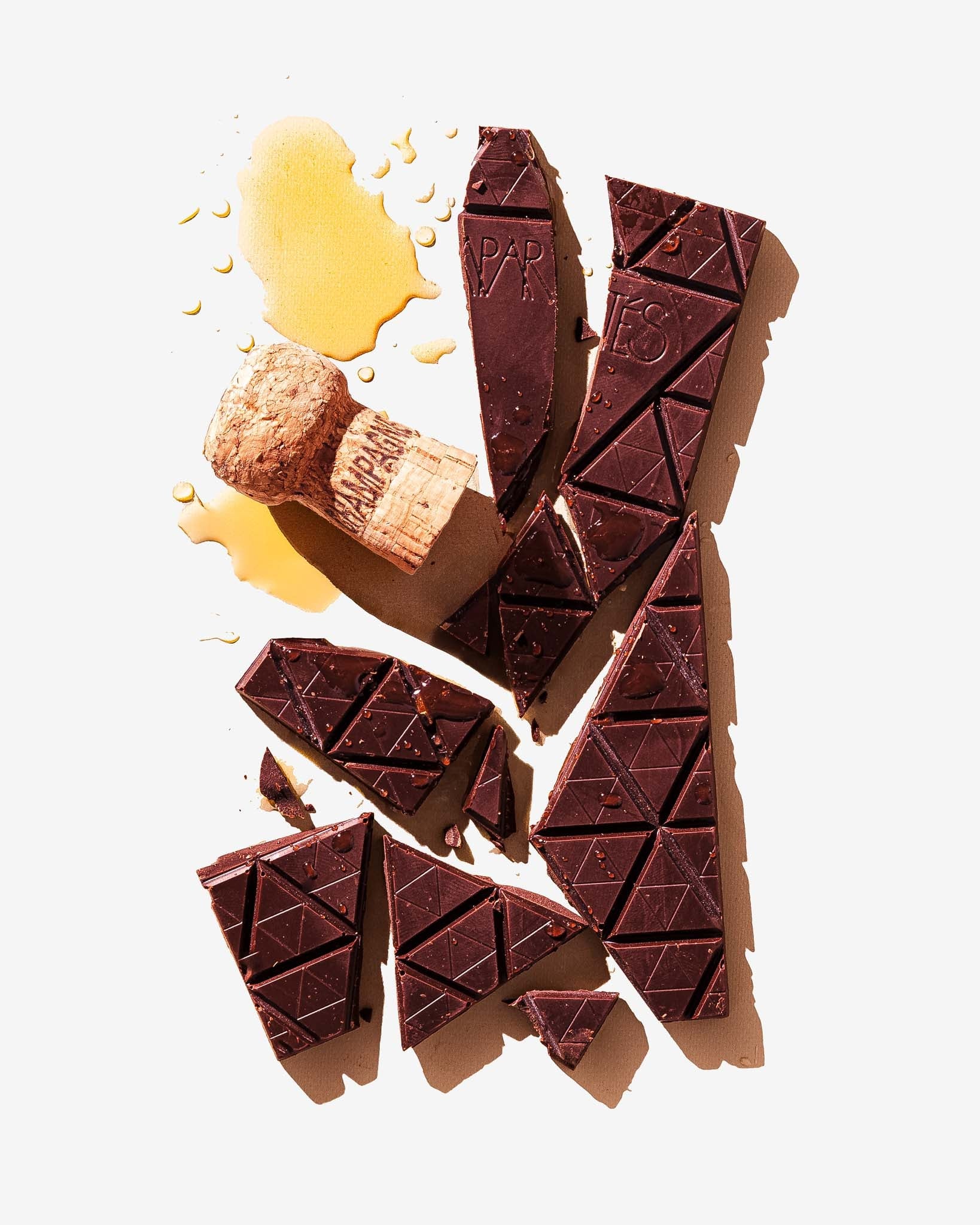 Chunks of a dark chocolate bar with a champagne cork and some champagne on a light background