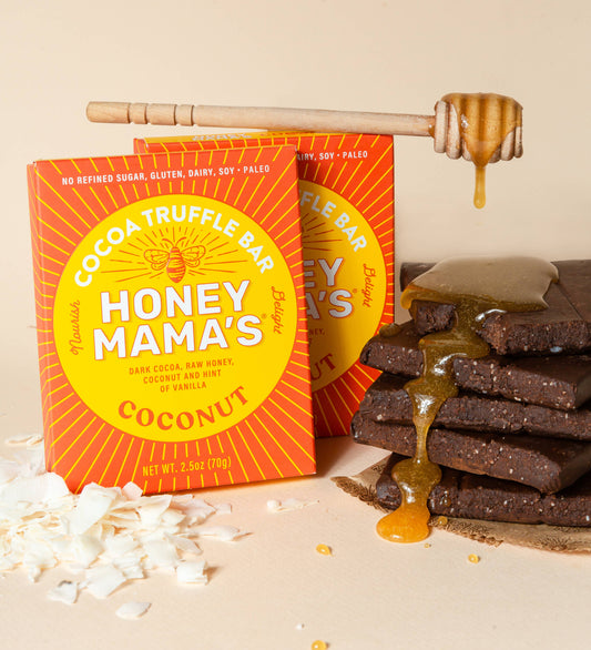 Packaging of Honey Mama's Coconut Cocoa Truffle Bar with the product visible next to it. On the packaging we can see that the bar is made from real foods only, paleo, refined sugar-free, dairy-free, and gluten-free. There is honey and shredded coconut in the setting.