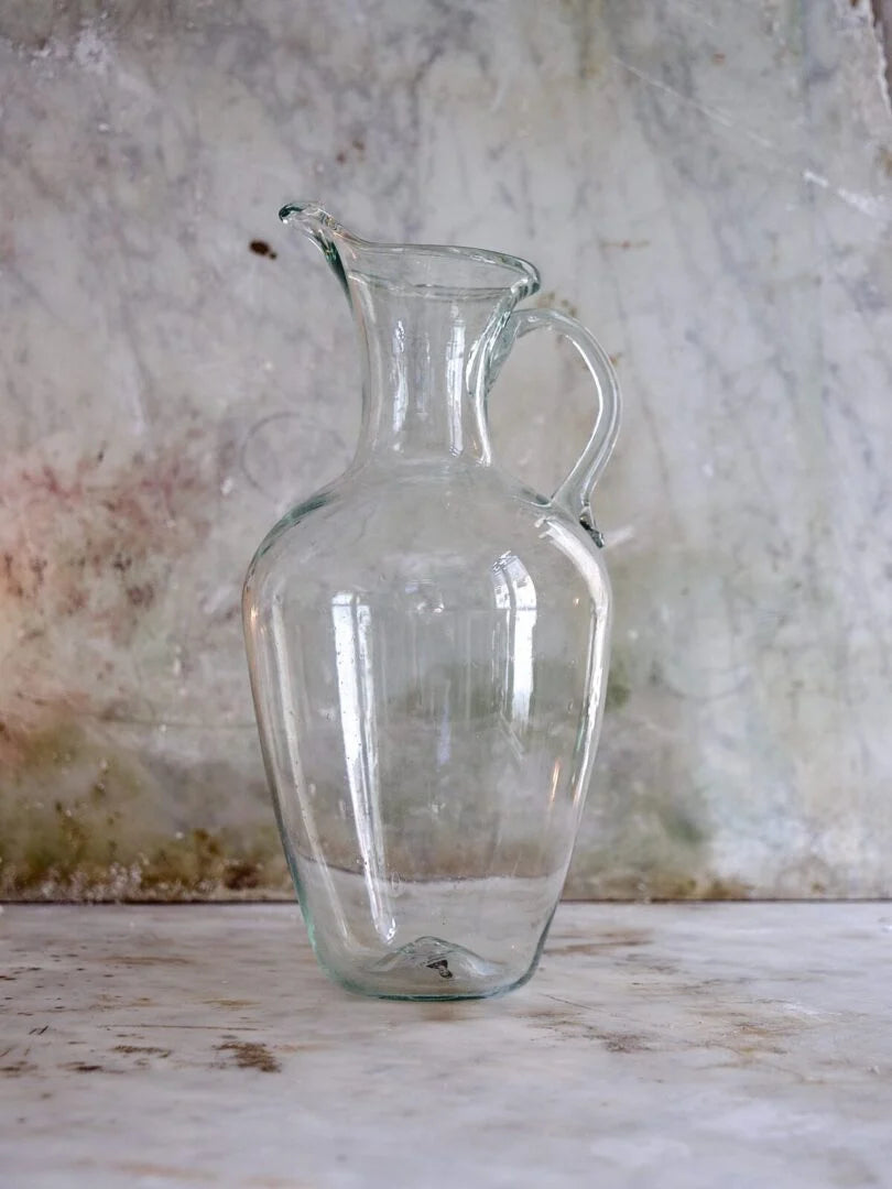 Clear glass pitcher on a textured surface with a neutral background