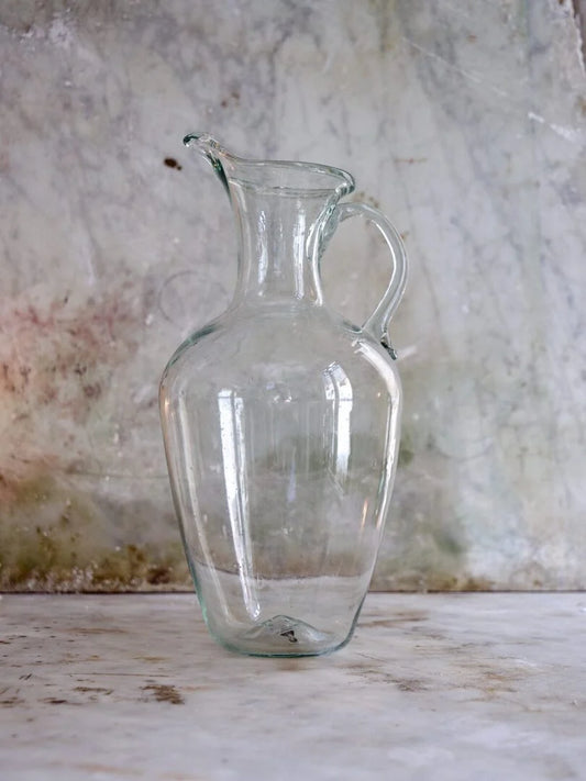 Clear glass pitcher on a textured surface with a neutral background