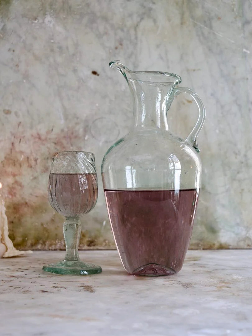 La Soufflerie Cruche mouth-blown glass jug and goblet with red liquid on a textured surface