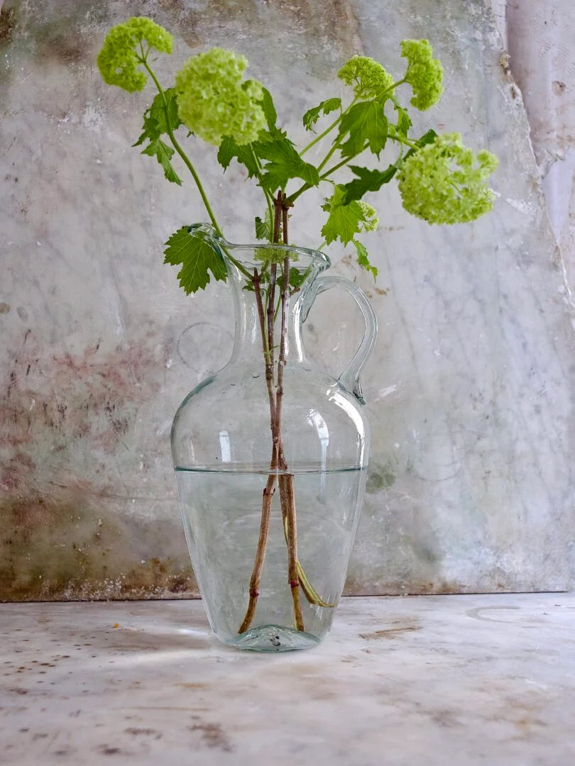 Clear and elegant glass vase with green flowers against a textured wall.
