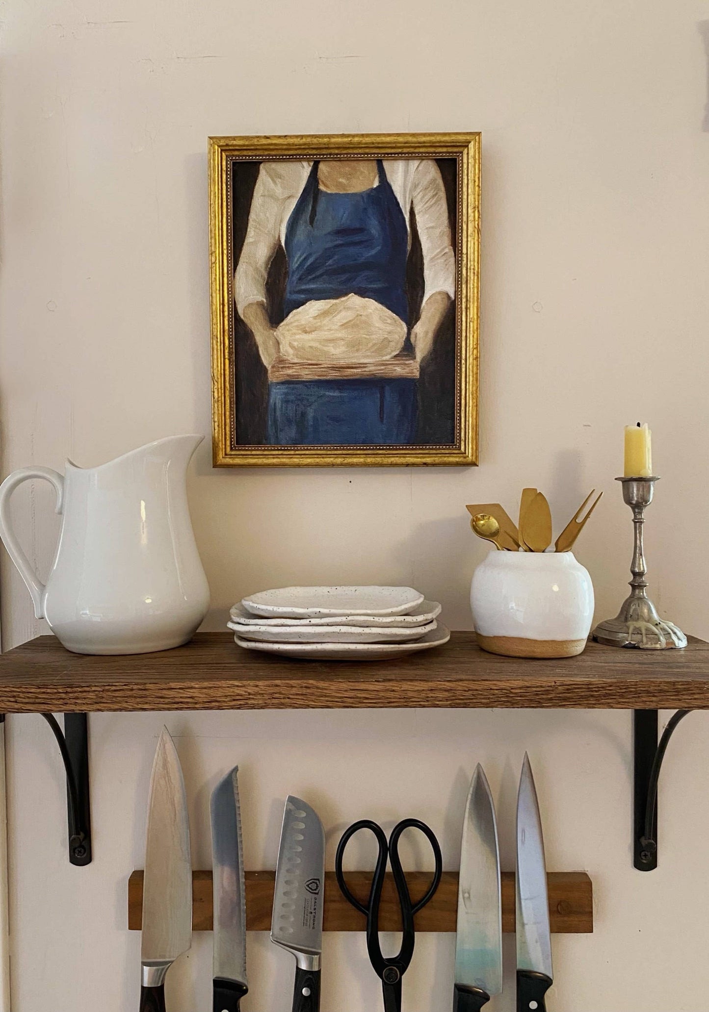 French-inspired art print of a woman holding sourdough bread, here hanged on a kitchen wall, with plates and cutlery beneath it.