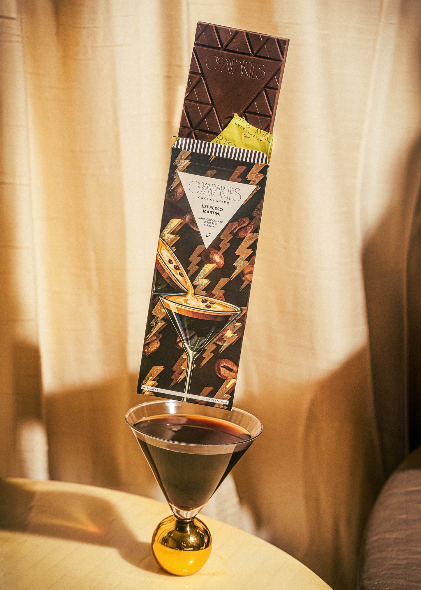 Dark Chocolate bar with cocktail design next to a glass of dark liquid on a textured surface