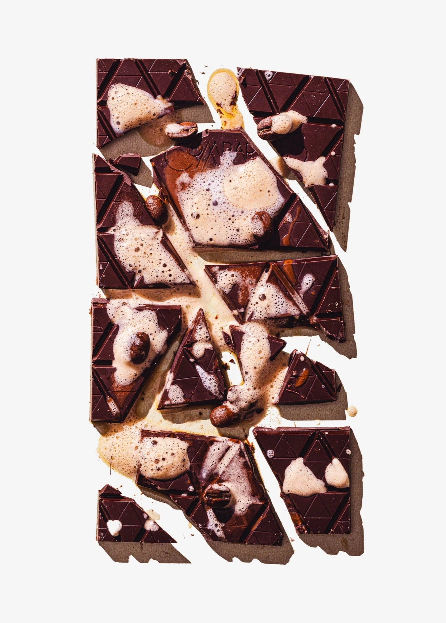 Chocolate bar chunked into pieces with a beverage on top on a light gray background