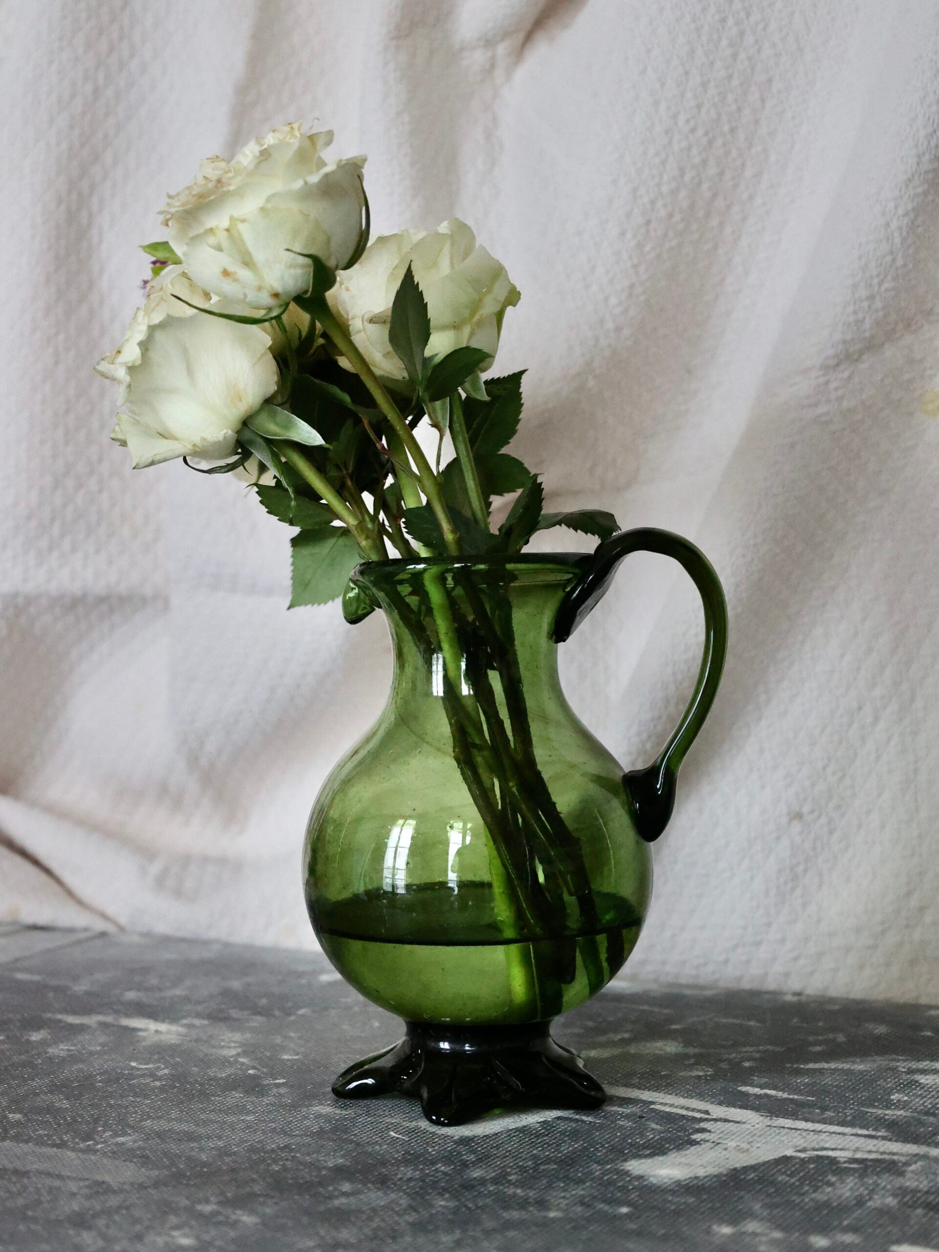 Elegant green glass vase with white roses against a white fabric background