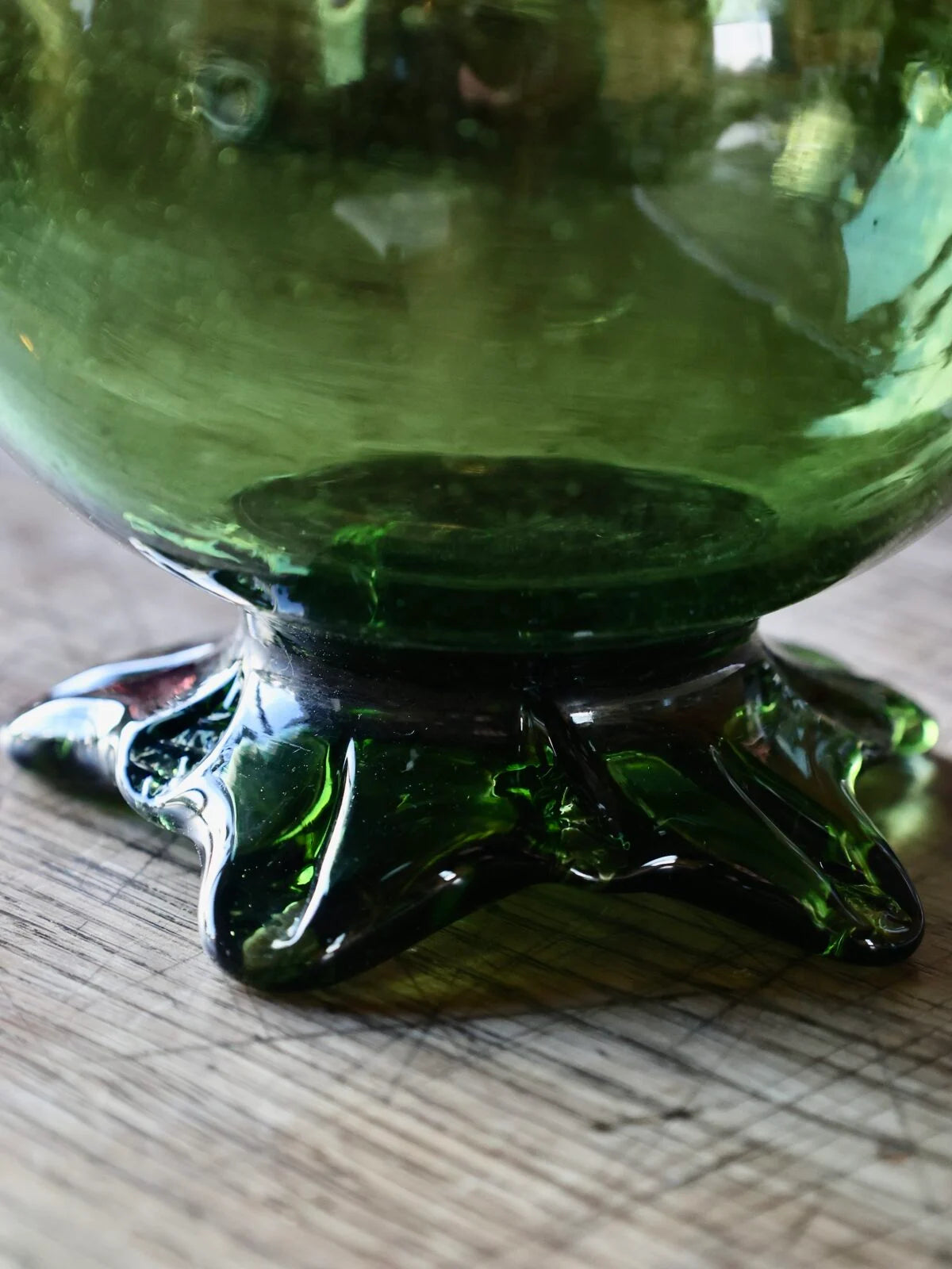 Bottom of a mouth-blown recycled green glass carafe inspired by Dionysos, with star-shaped base on a wooden surface