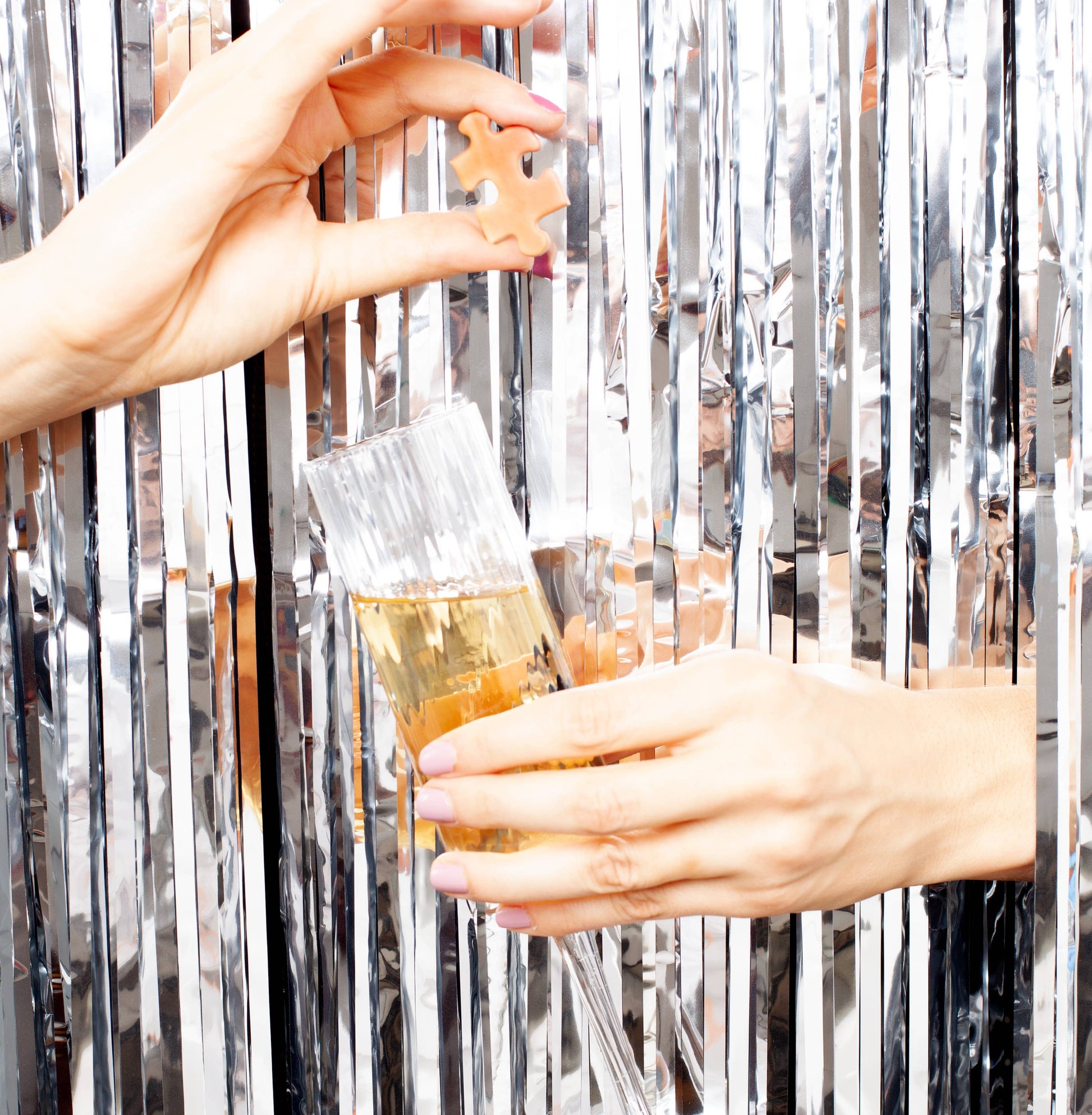 Hands holding a glass full and a piece of puzzle, in a disco setting.