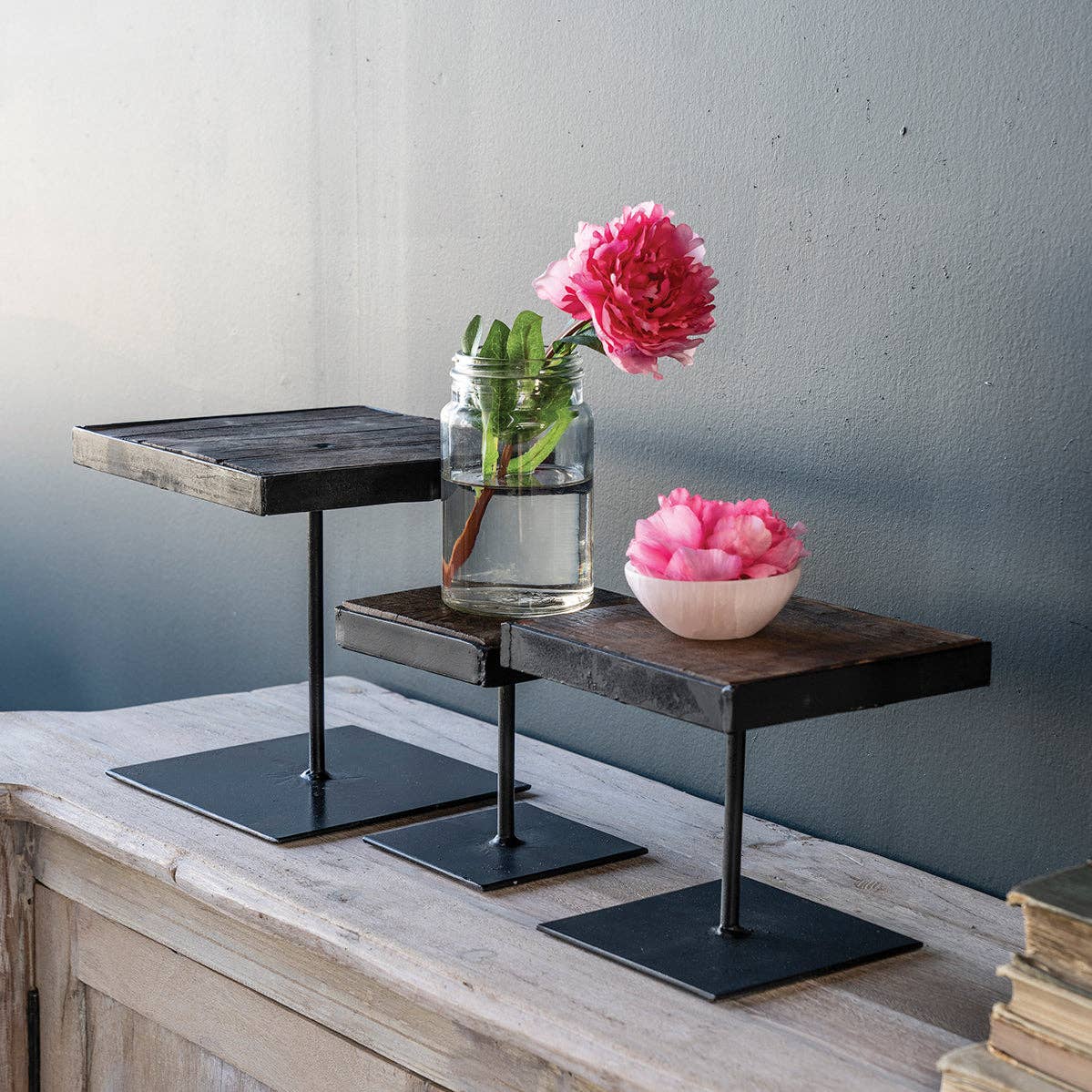 Black iron display risers with wood top, small, medium and large versions, with pink flowers on top.