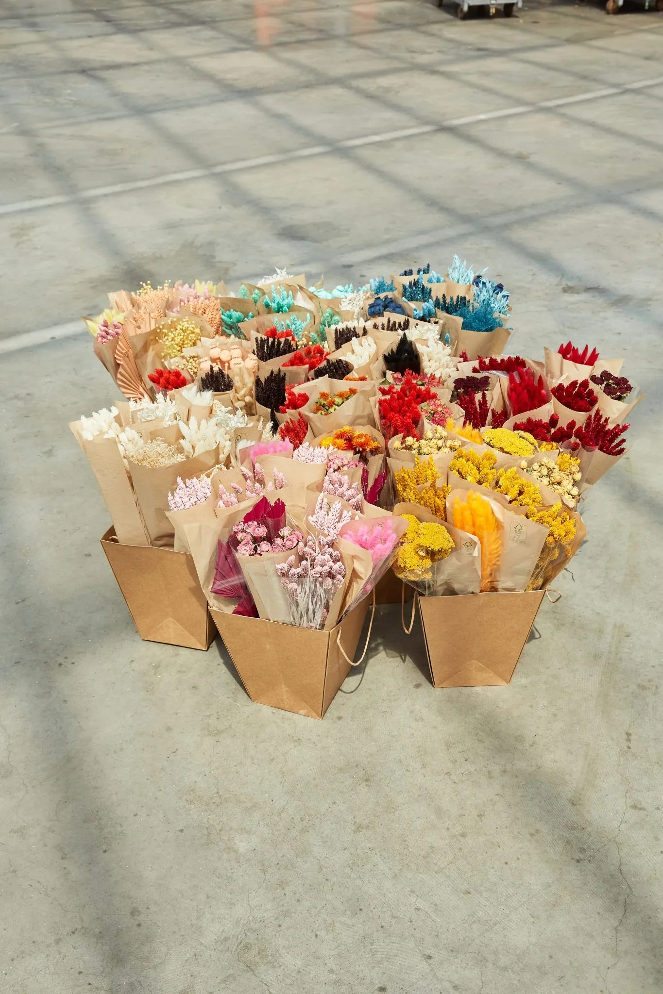 Assorted bouquets of natural dried flowers in brown paper bags on a concrete floor.