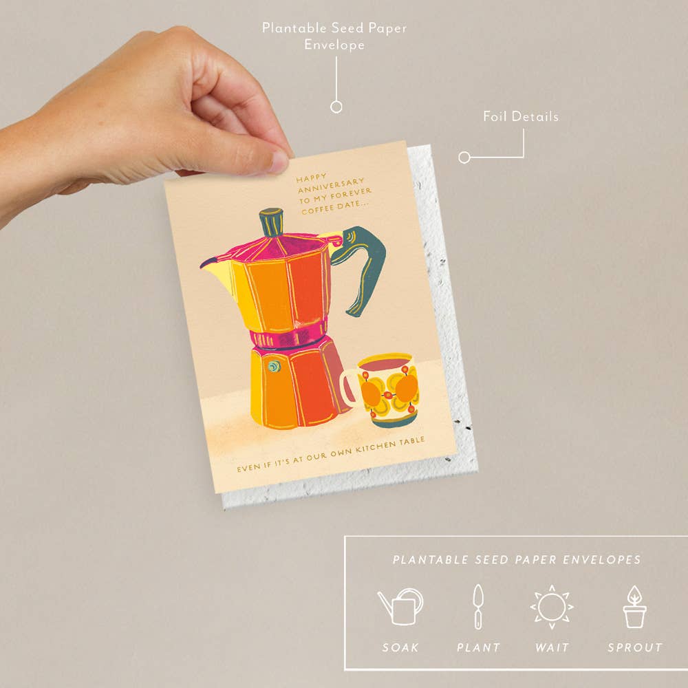 A hand holding a greeting card with illustration of a red and yellow espresso maker and a colorful vintage cup, with text celebrating an anniversary. Accompanied by a plantable seed paper envelope with eco-friendly packaging details.