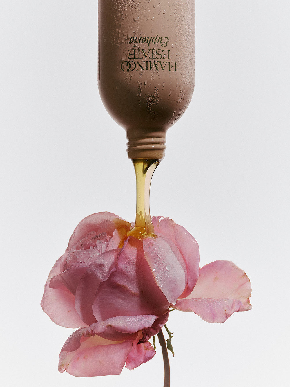 Bottle of Flamingo Estate Euphoria Hand soap being poured onto a pink rose on a light gray background