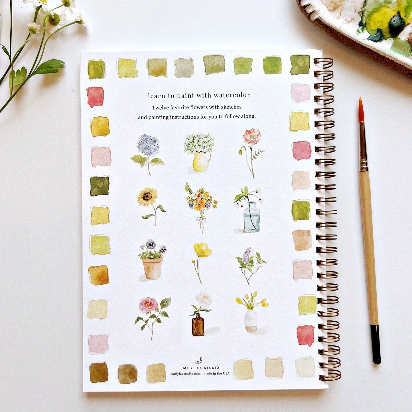 Flowers Watercolor Workbook with floral illustrations, color swatches and spiral binding. A watercolor brush is lying next to the book.