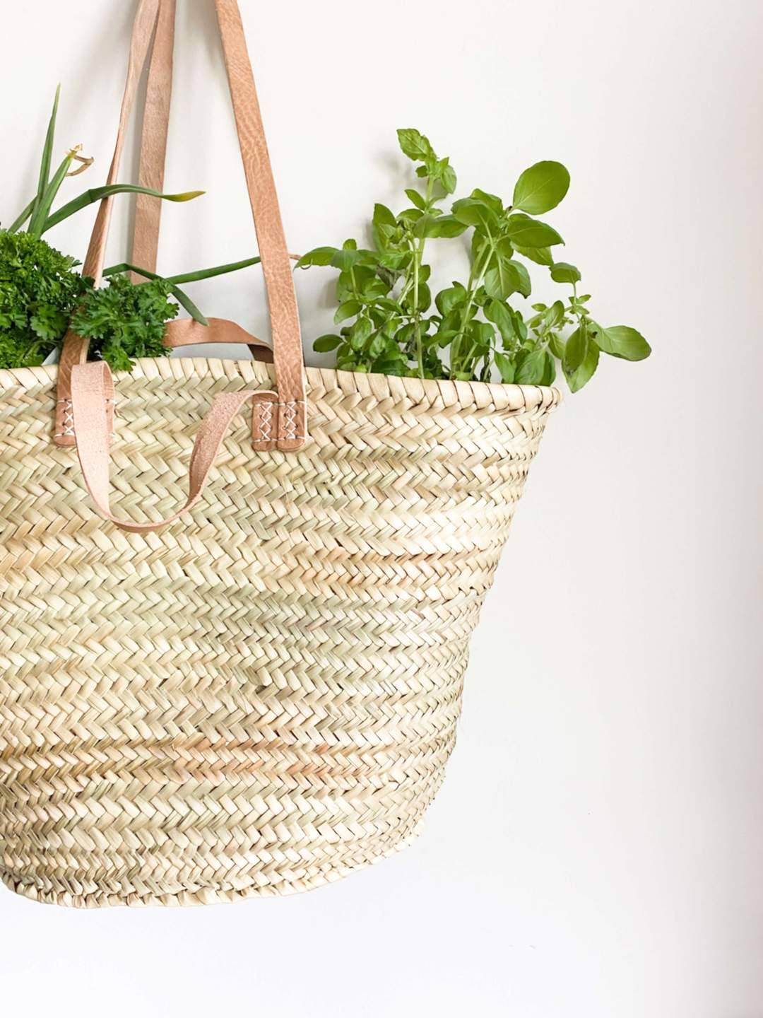 Artisanal woven straw market basket with plants on a white background