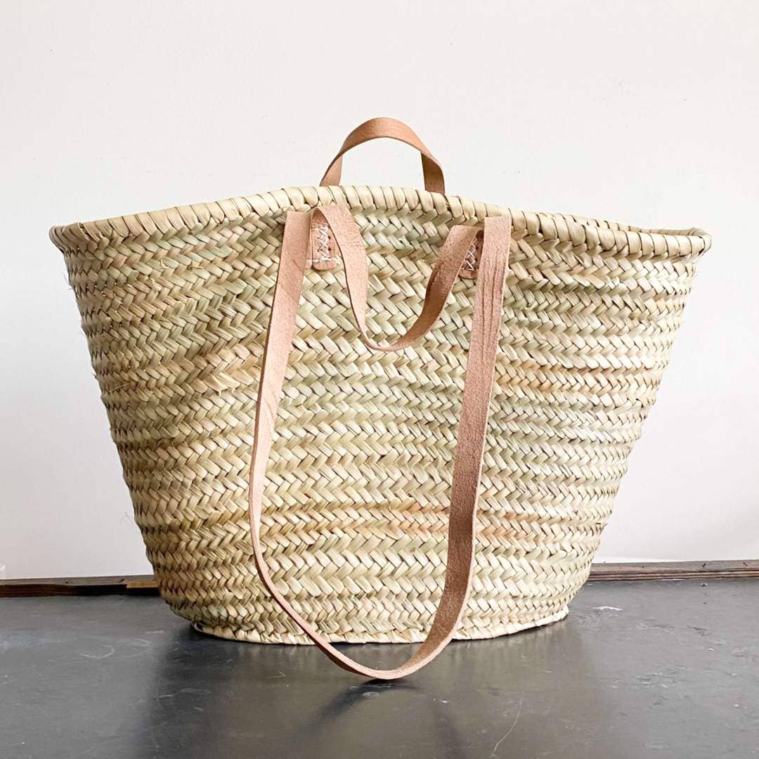 handwoven straw french market basket with leather handles on a plain background