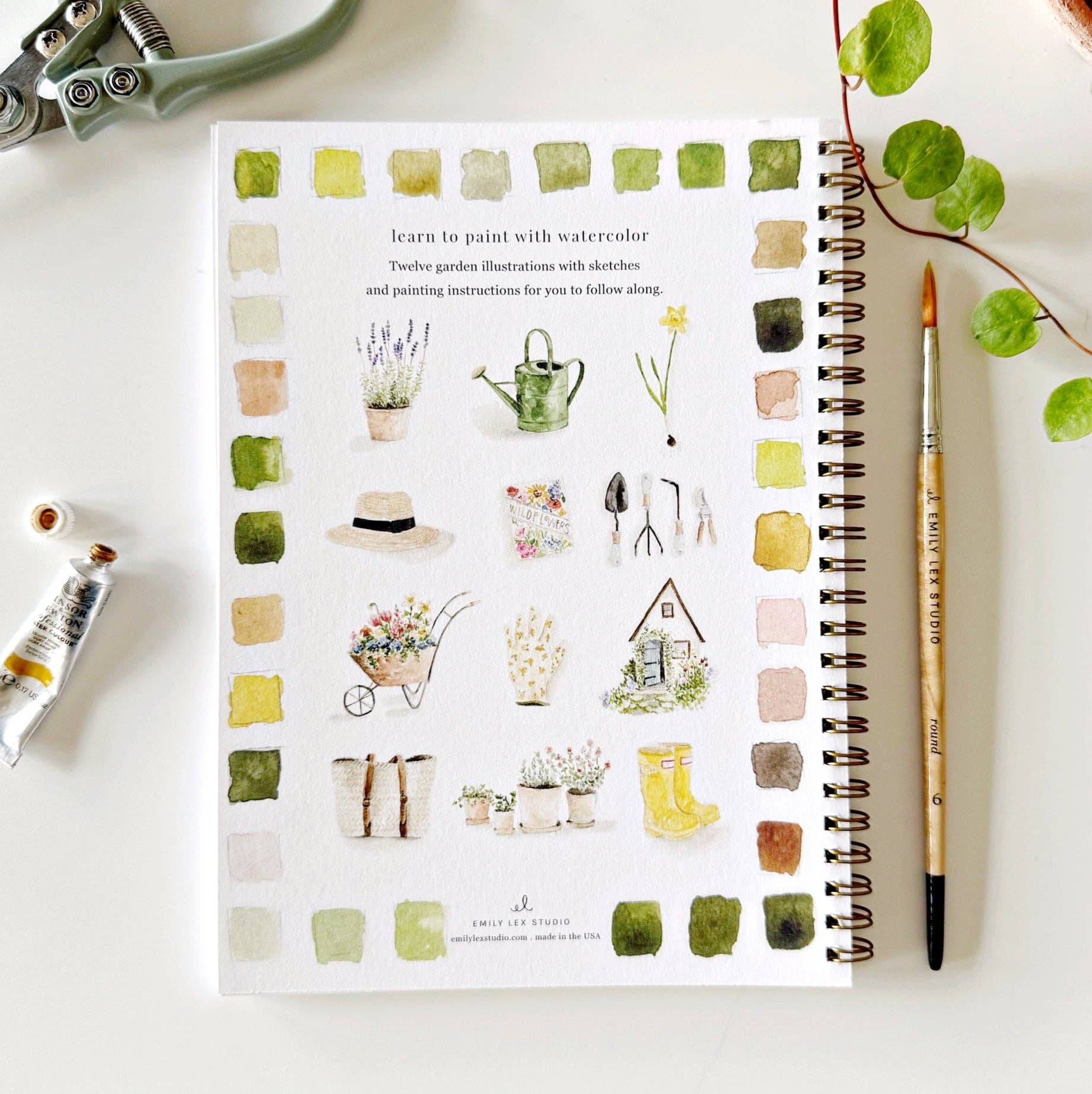 Garden Watercolor Workbook with illustrations from the garden, color swatches and spiral binding. A watercolor brush is lying next to the book.