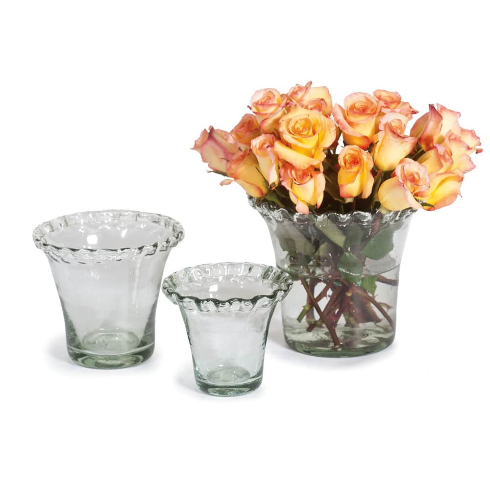 Set of three clear glass vases with a pie crust shape and a bouquet of peach-colored roses on a white background
