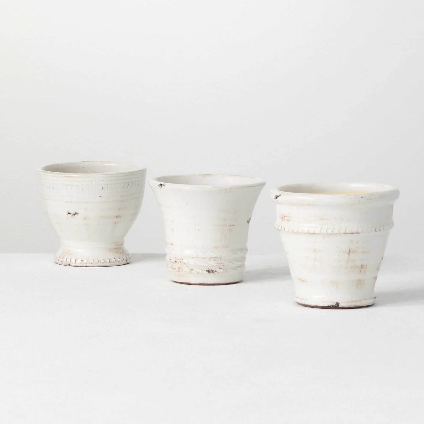 Three small white glazed ceramic pots with elegant details.