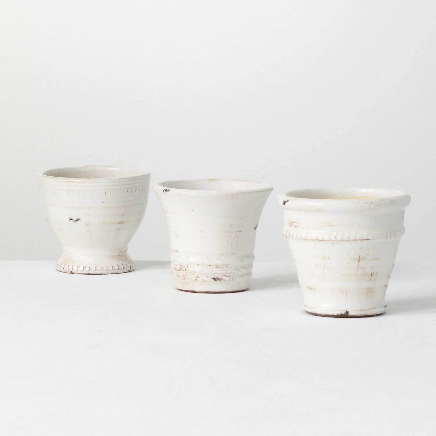 Three small white glazed ceramic pots with elegant details.