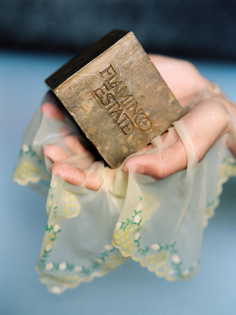 Hand holding a Green Goddess bar of soap with 'Flamingo Estate' branding against a blue background