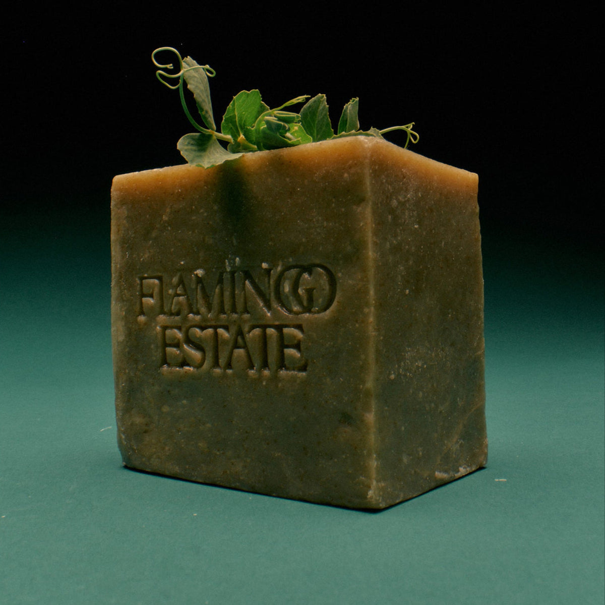 Square block of Green Goddess herbal bar soap with basil and mint, with 'Flamingo Estate' branding on a green background