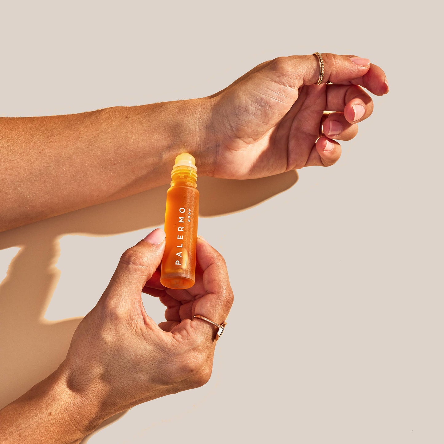 Hand holding a bottle labeled 'Palermo', a geranium, white lotus and cedarwood natural perfume oil, against a neutral background