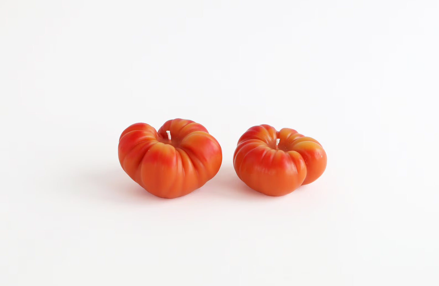 Two orange tomatoes beeswax candles on a white background