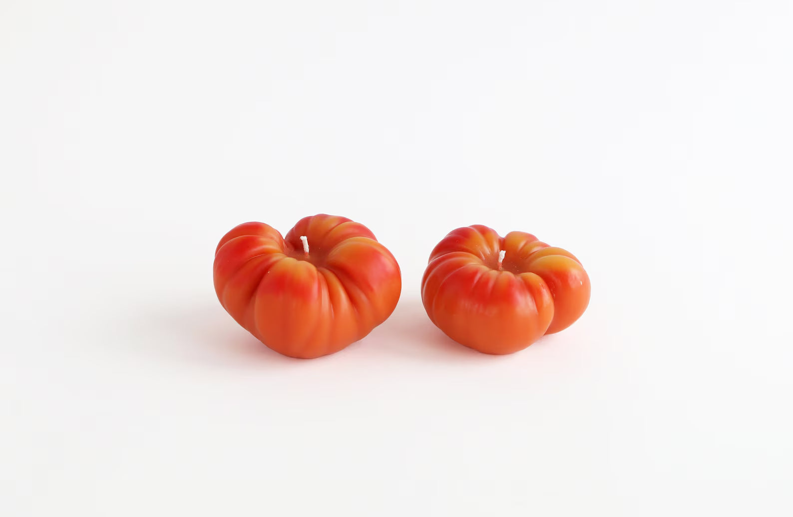 Two orange tomatoes beeswax candles on a white background